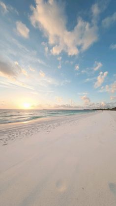 the sun is setting on an empty beach with footprints in the white sand and blue water