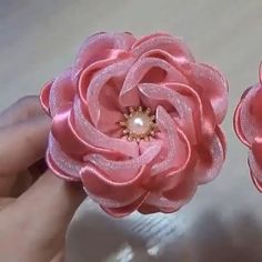 two pink flowers with pearls in the center being held by someone's hand on a table