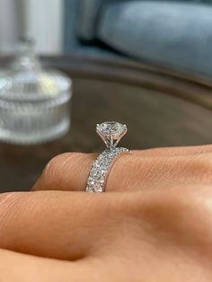 a woman's hand with a diamond ring on top of her finger in front of a glass table