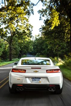 the back end of a white car driving down a road with trees in the background