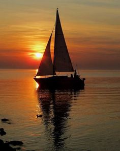 a sailboat floating on top of a body of water under a cloudy sky at sunset