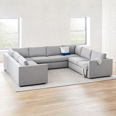 a living room with a large sectional couch and pillows on the floor in front of two windows