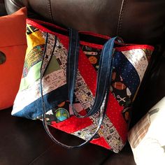 a multicolored bag sitting on top of a brown leather couch next to an orange pillow