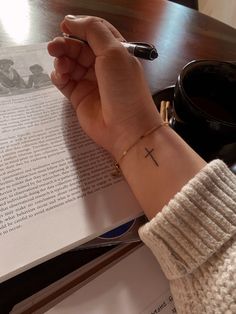 a person with a cross tattoo on their wrist is holding a pen and reading a book