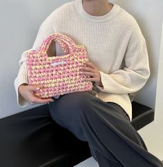 a woman sitting on a bench holding a pink and white purse in front of her face