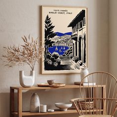 an art print hangs on the wall above a wooden table with white dishes and vases