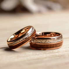 two gold wedding rings with engraved designs on them sitting on a wooden table next to each other