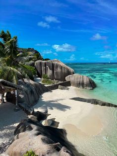 the beach is surrounded by palm trees and clear blue water, as well as large boulders