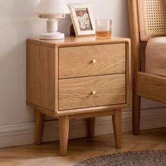 a wooden night stand with two drawers and a lamp on top of it next to a bed