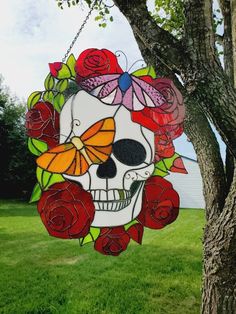 a stained glass skull hanging from a tree with roses and butterflies on it's face