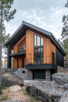 a modern house with wood and glass on the front, surrounded by rocks and trees