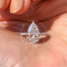 a woman's hand holding an engagement ring with a pear shaped diamond