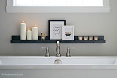 a bathroom sink with candles and pictures on the shelf above it in front of a window