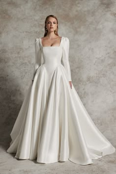 a woman in a white wedding dress with long sleeves and an open back, standing against a