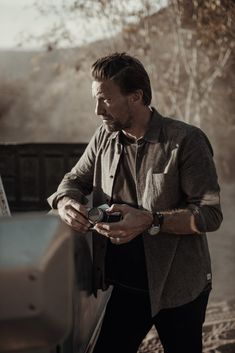 a man standing next to a car looking at his cell phone while wearing a watch