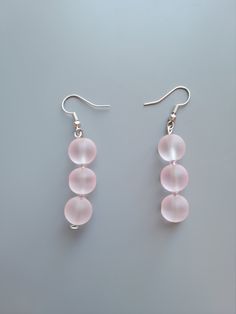 three pink glass beads hang from silver earwires on a gray surface, with one bead in the middle