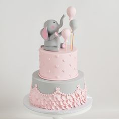 there is a pink and grey cake with an elephant on top that has balloons in the air