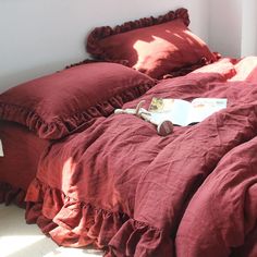 the bed is made with red linens and ruffled pillows, along with a book on it