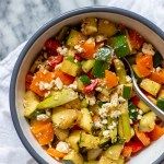 a bowl filled with chopped vegetables on top of a marble countertop next to a spoon