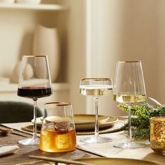 three wine glasses sitting on top of a wooden table next to plates and utensils