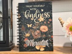 a note book sitting on top of a wooden table next to a vase with flowers