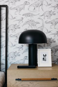 a black lamp sitting on top of a wooden table next to a wall with dinosaurs