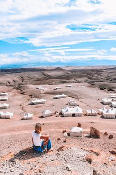 a woman sitting on top of a hill next to a desert town in the distance