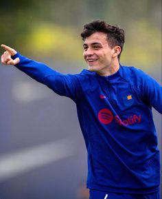 a soccer player is pointing to the side with his arm out and smiling while wearing a blue uniform