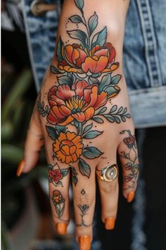 a woman's hand with tattoos and flowers on her left hand, which is decorated with gold rings