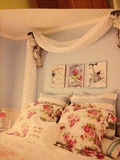 a bed with white sheets and pink flowers on the comforter next to two framed pictures