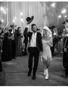 a man and woman walking through a crowd holding sparklers