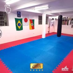 an indoor boxing gym with blue mats and punching bags on the wall, in front of several flags