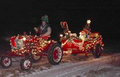 two red tractors decorated with christmas lights on the side of a snow covered road at night