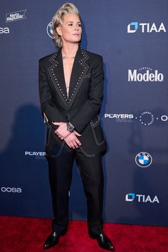 a woman in a black suit standing on a red carpet with her hands behind her back