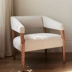 a white chair sitting on top of a hard wood floor next to a window with curtains