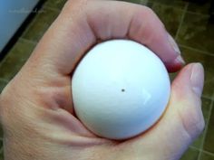 a person holding an egg in their hand on a tile flooring area behind them