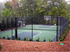 an outdoor basketball court surrounded by trees and bushes in the fall or winter with leaves on the ground