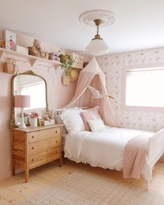 a bedroom decorated in pink and white with a bed, dresser, mirror and window