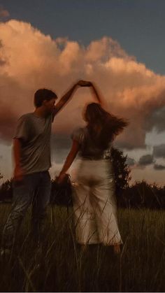 a man and woman dancing in a field with the sun setting behind them, as clouds loom overhead