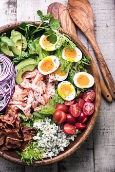 a wooden bowl filled with meat, veggies and eggs on top of a table