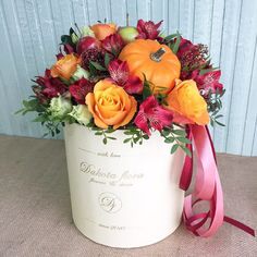 an orange and red flower arrangement in a white box with a pink ribbon around it