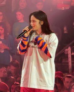 a man with long hair holding a microphone in front of a large group of people