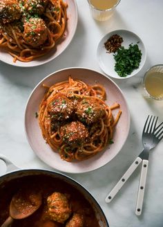 two plates of spaghetti and meatballs on a white table with silver utensils