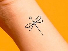 a small black dragonfly tattoo on the left inner arm and wrist, with an arrow in the middle