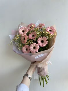 a person holding a bouquet of pink daisies and baby's breath in their hand