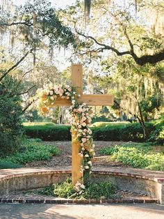 a wooden cross with flowers on it sitting in the middle of a park surrounded by trees