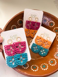 four pairs of earrings are sitting on a brown plate with white and blue circles around them