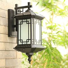 an outdoor light hanging on the side of a brick wall next to a planter