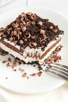 a white plate topped with a piece of cake covered in whipped cream and chocolate chips