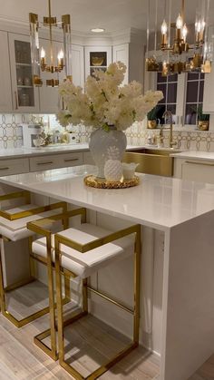 a large white kitchen with gold accents and chandeliers